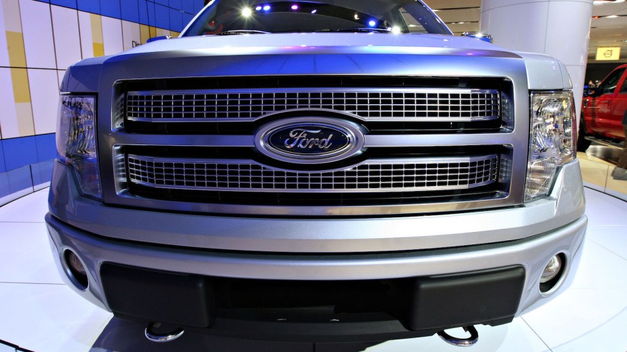 The grille of a silver Ford F-150 pickup truck parked on the stage at an auto show.