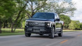 A black Ford F-150 Lightning Platinum all-electric pickup truck model driving on a country highway