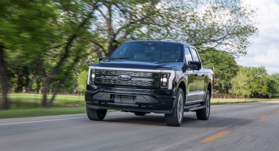 A model black Ford F-150 Lightning Platinum all-electric pickup truck being driven on a country road