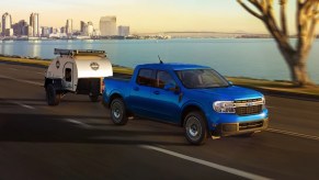 A blue Ford Maverick small pickup truck is driving on the road.