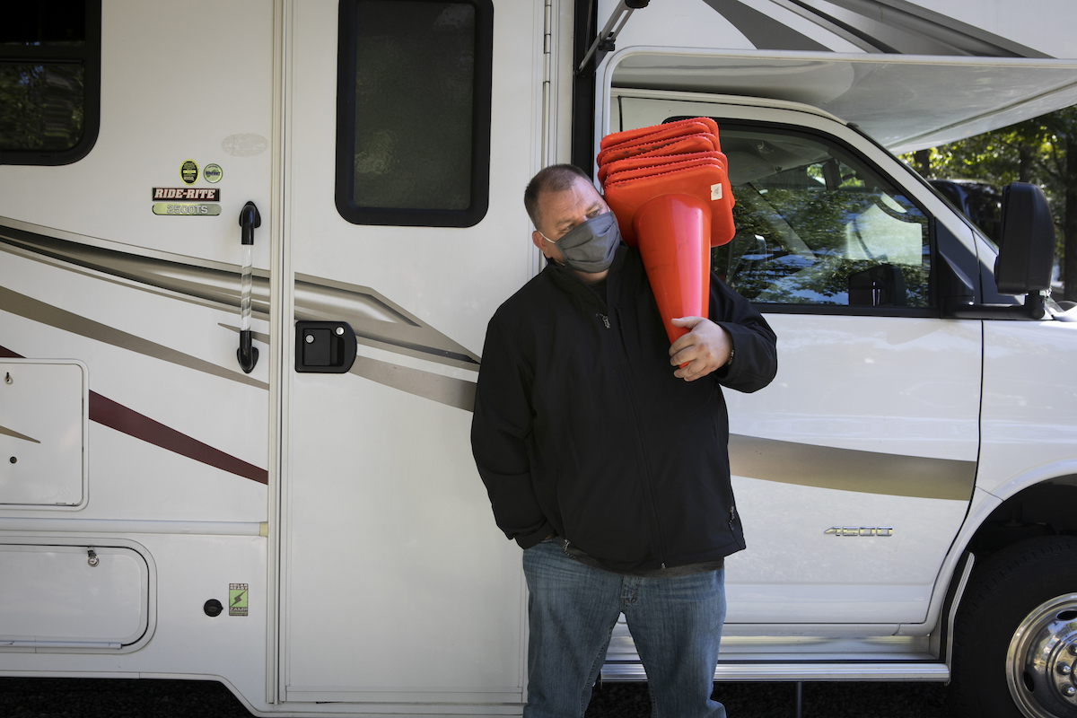 A person carrying cones in front of an RV, potentially for indoor RV storage.