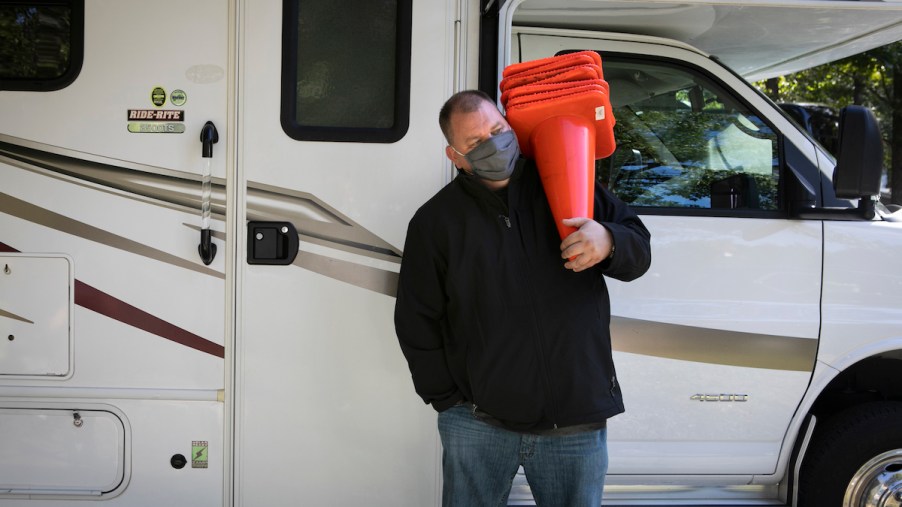 A person carrying cones in front of an RV, potentially for indoor RV storage.
