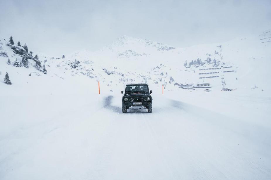 Promo photo of the Land Rover Defender based Ineos Grenadier SUV driving down a snow-covered road, mountains visible in the background.
