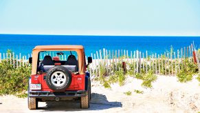 A red Jeep Wrangler YJ parked on the beach, a blue ocean visible in the background.