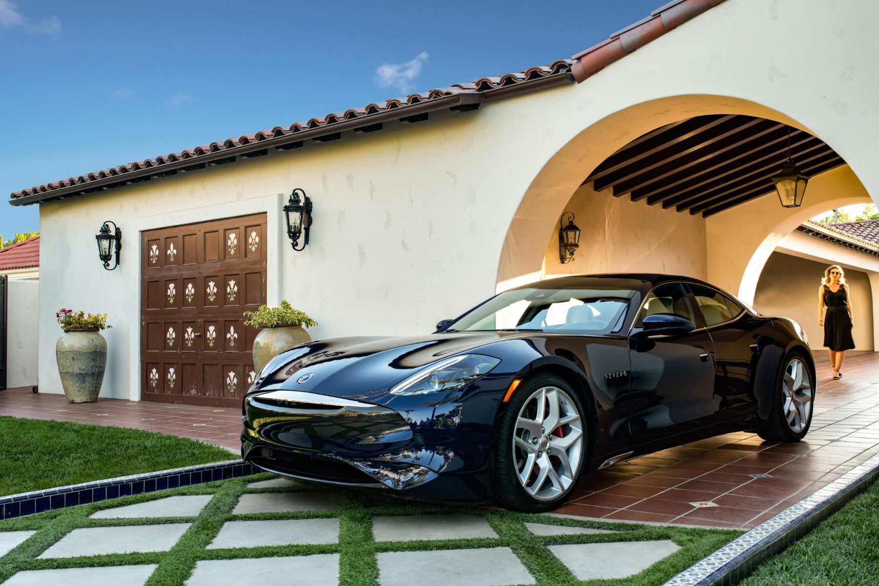 A black Karma Revero GT plug-in hybrid electric vehicle (PHEV) parked on the brick driveway of a luxury home