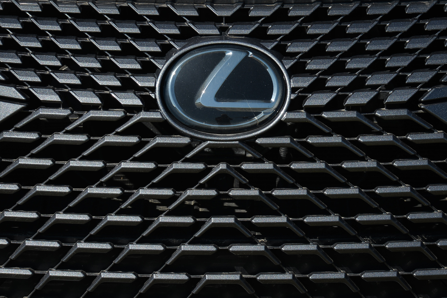 The Lexus logo on the grille of a crossover luxury SUV parked at a used vehicle dealership.