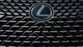 The Lexus logo on the grille of a crossover luxury SUV parked at a used vehicle dealership.