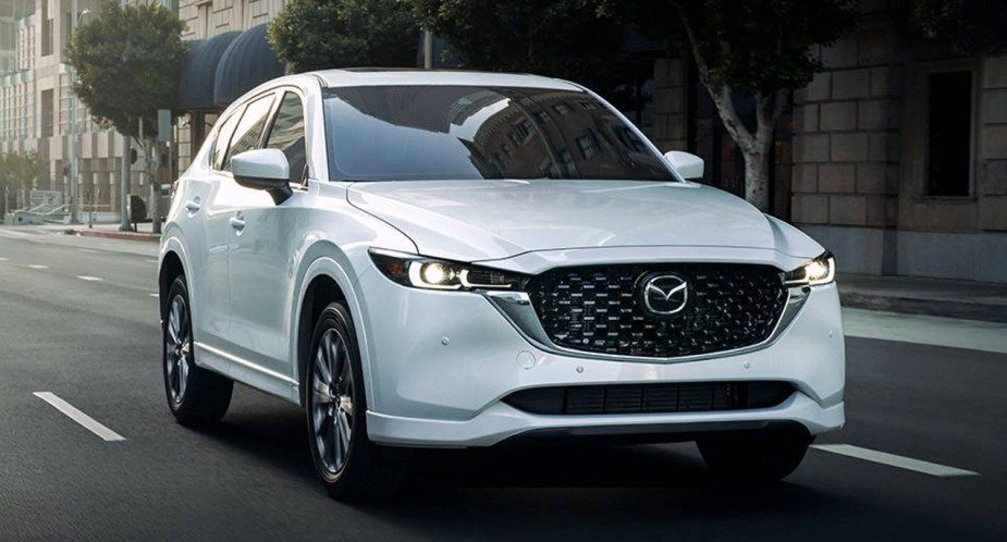 A white 2023 Mazda CX-5 small SUV is driving on the road. 