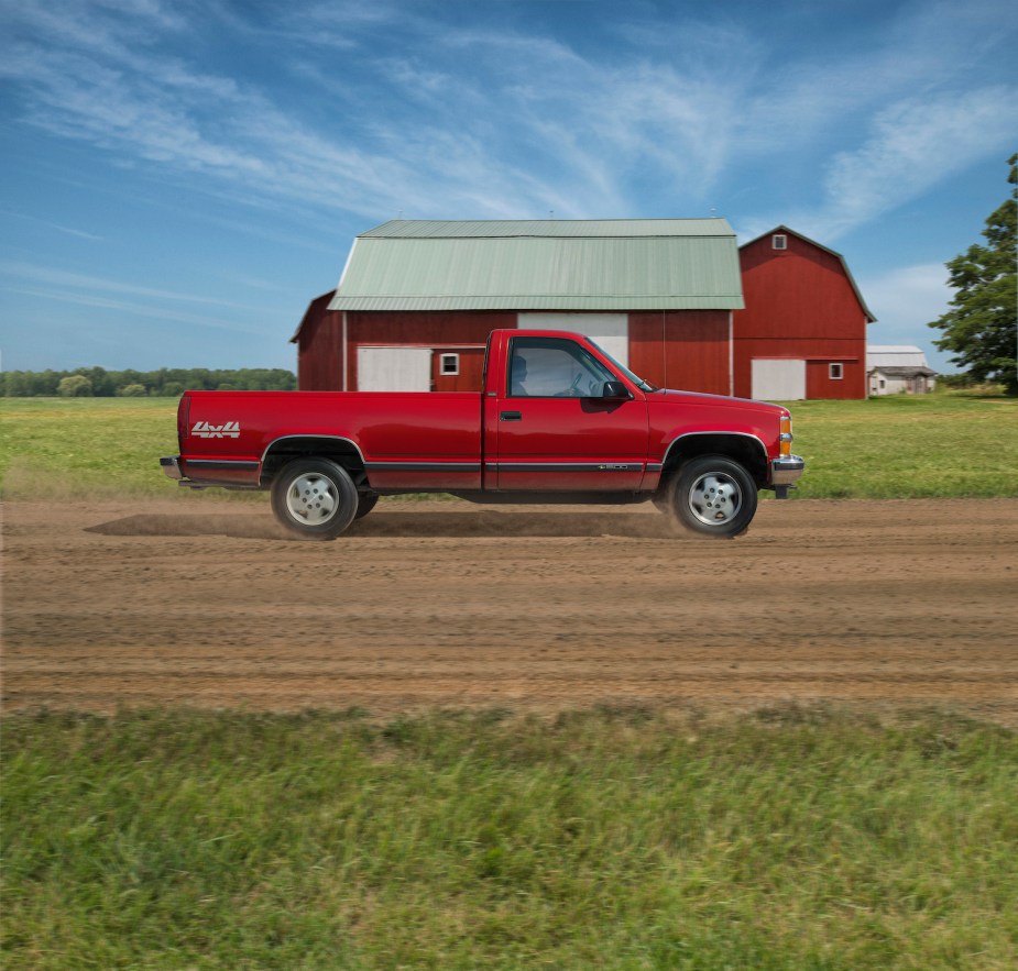 Image of a red Chevrolet K1500 pickup truck driving through a patch of dirt on a farm, the barn visible in the background.
