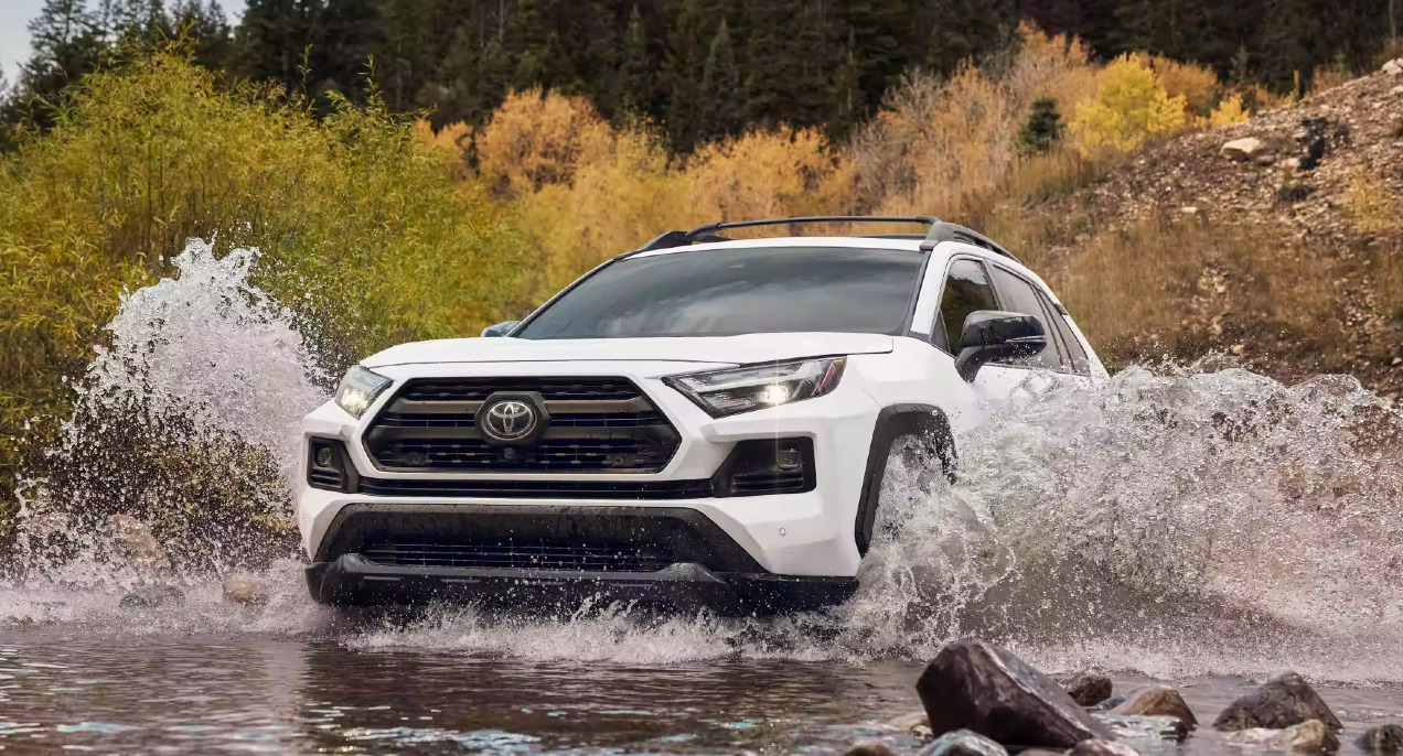 A white 2023 Toyota RAV4 is driving through the water.