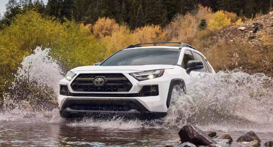 A white 2023 Toyota RAV4 small SUV is driving through water. 