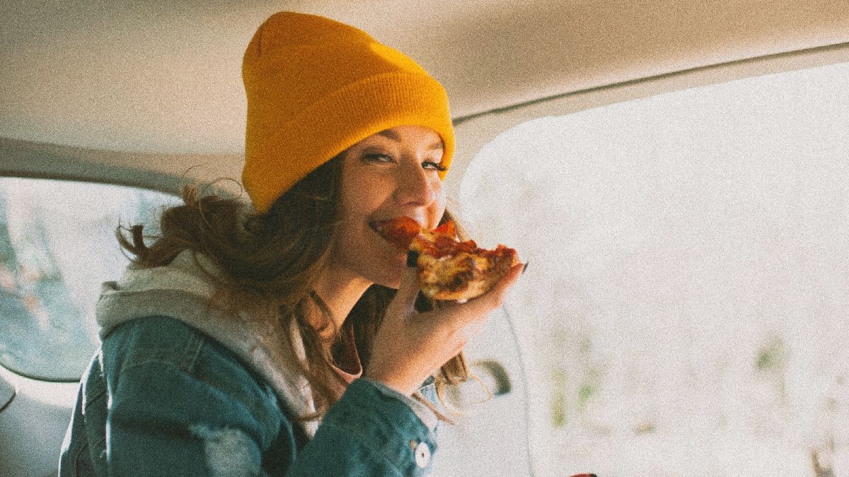 Woman eating a pizza in a vehicle, highlighting how to eat food in a car without making a mess