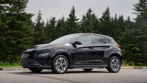 A black 2023 Hyundai Kona Electric all-electric (EV) compact SUV model parked near a forest of evergreen trees