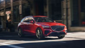A red Genesis GV70 compact crossover luxury SUV model driving through a city