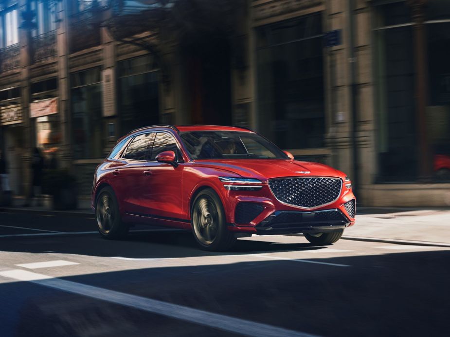 A red Genesis GV70 compact crossover luxury SUV model driving through a city Consumer Reports now recommends.