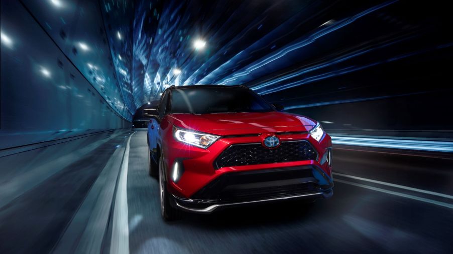 A red Toyota RAV4 Prime plug-in hybrid electric vehicle (PHEV) driving through a lighted tunnel