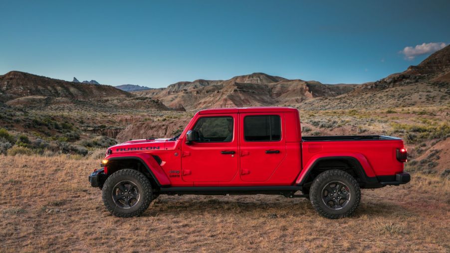 A side profile shot of a red 2023 Jeep Gladiator Rubicon midsize pickup truck parked in the wilderness