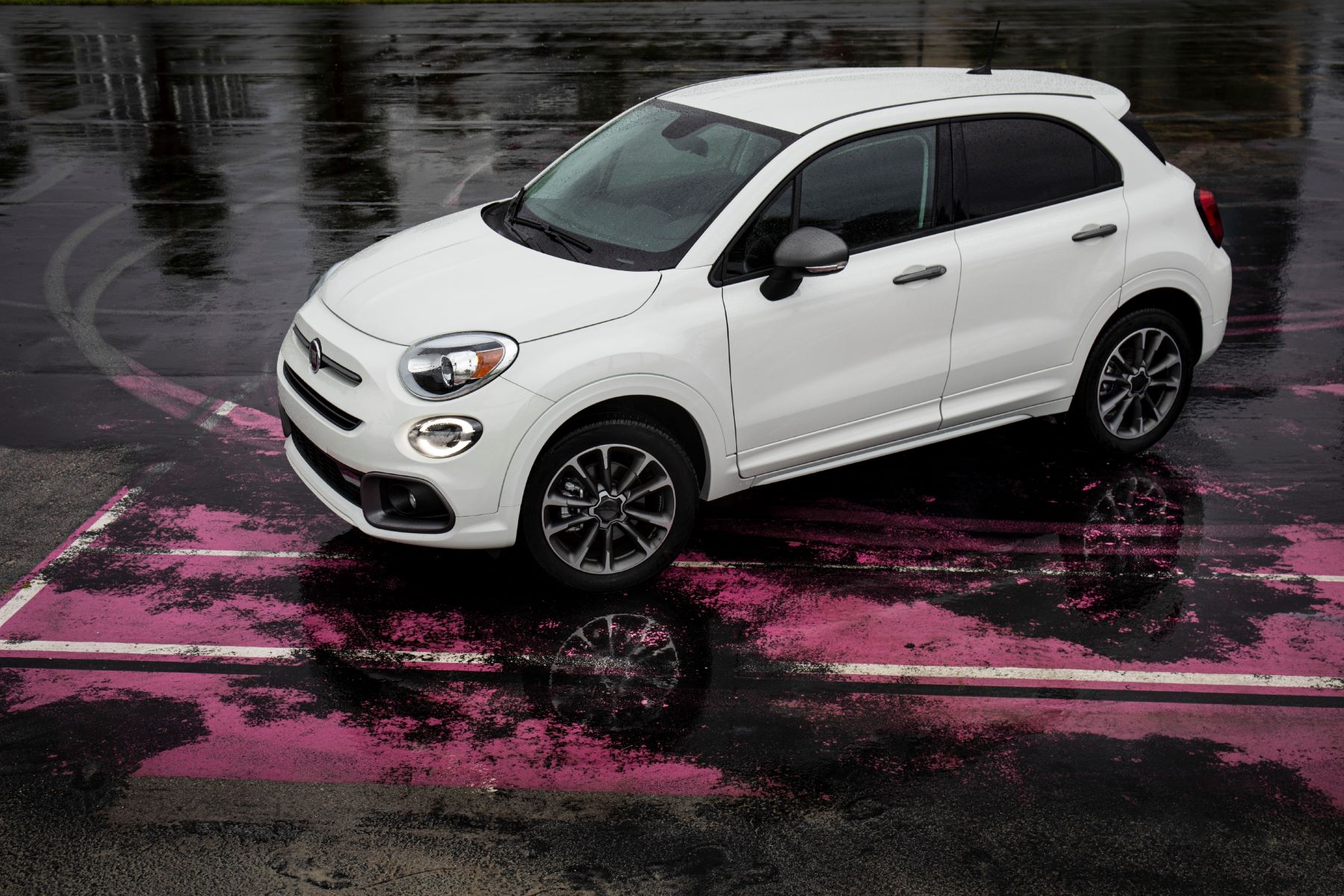 A white 2023 Fiat 500X subcompact crossover SUV parked on a wet parking lot with worn pink paint