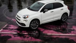 A white 2023 Fiat 500X subcompact crossover SUV parked on a wet parking lot with worn pink paint