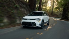 A white 2023 Kia Niro EV electric compact SUV model driving on a winding forest highway