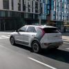 A white 2023 Kia Niro EV electric compact SUV model driving through an urban city near a set of streetlights