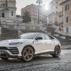 A white Lamborghini Urus Ambient luxury SUV model parked on black cobblestone before marble staircases