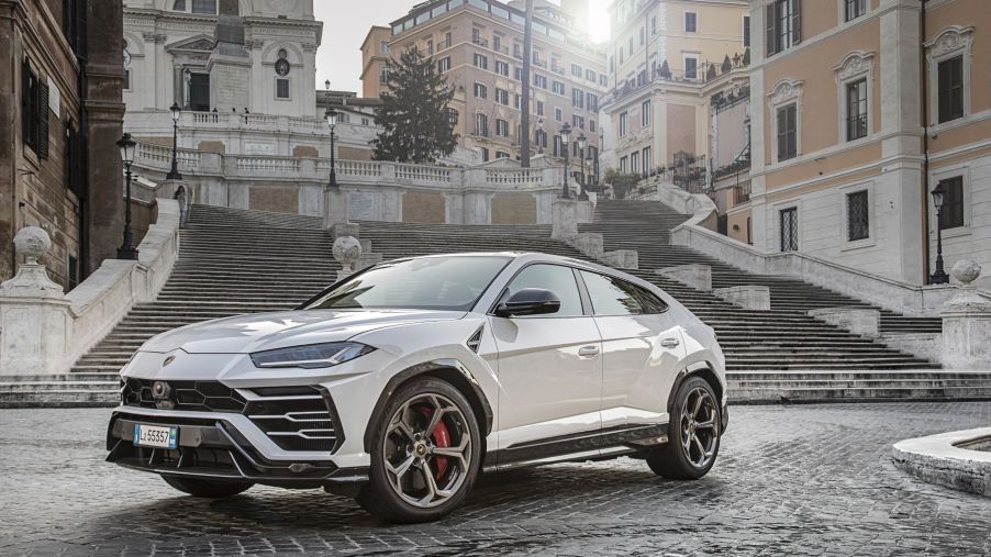 A white Lamborghini Urus Ambient luxury SUV model parked on black cobblestone before marble staircases