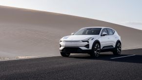 A white Polestar 3 all-electric luxury SUV on a shiny black highway near a sand dune