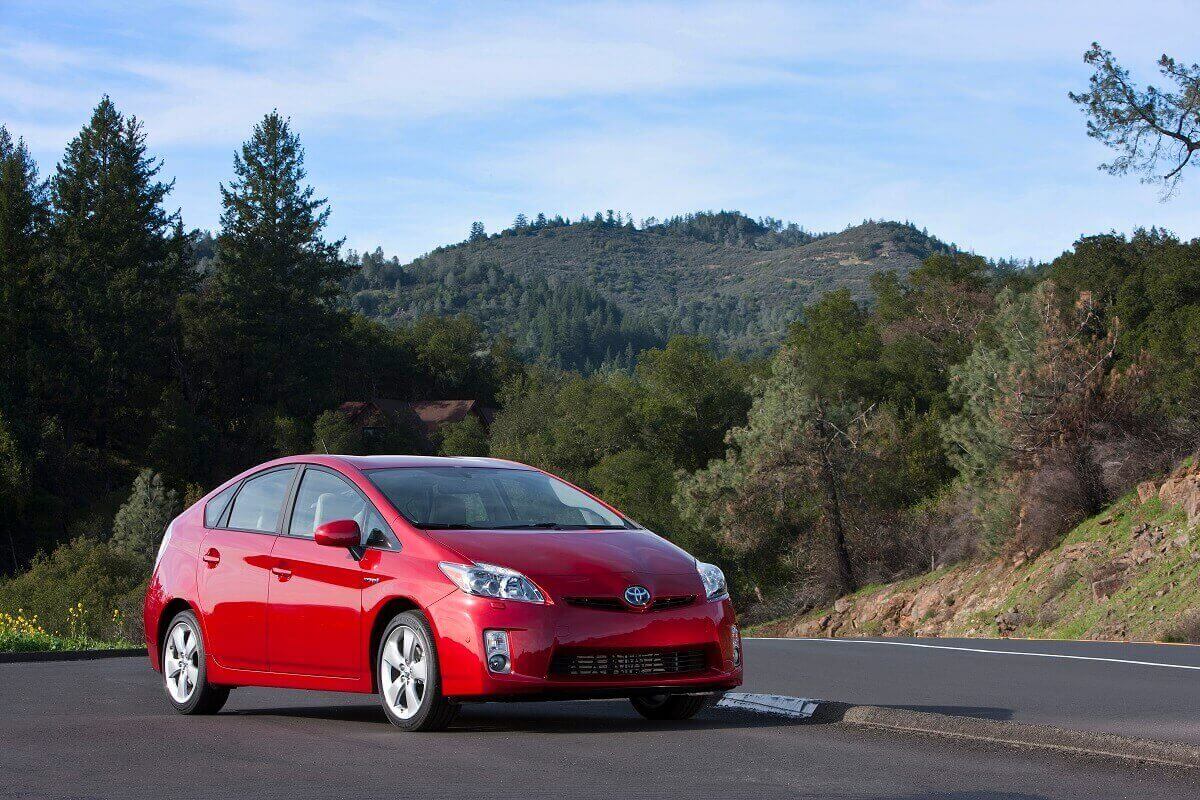 A red Toyota Prius parks next to a forest.