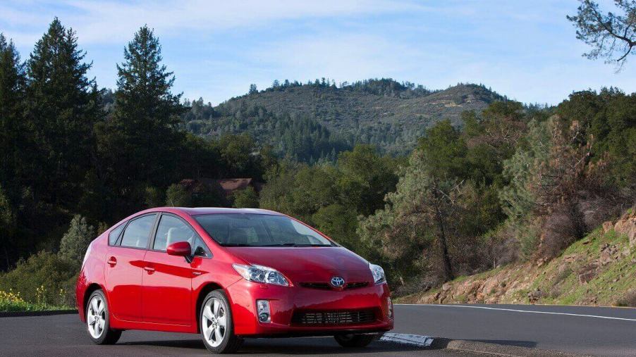 A red Toyota Prius parks next to a forest.