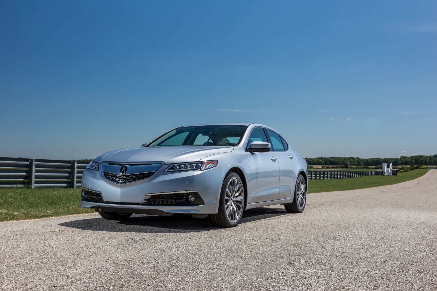 A 2015 Acura TLX entry-level luxury sedan model parked on a gravel road near metal fencing on a farm
