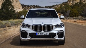 A white 2018 BMW X5 midsize luxury SUV is driving on the road.
