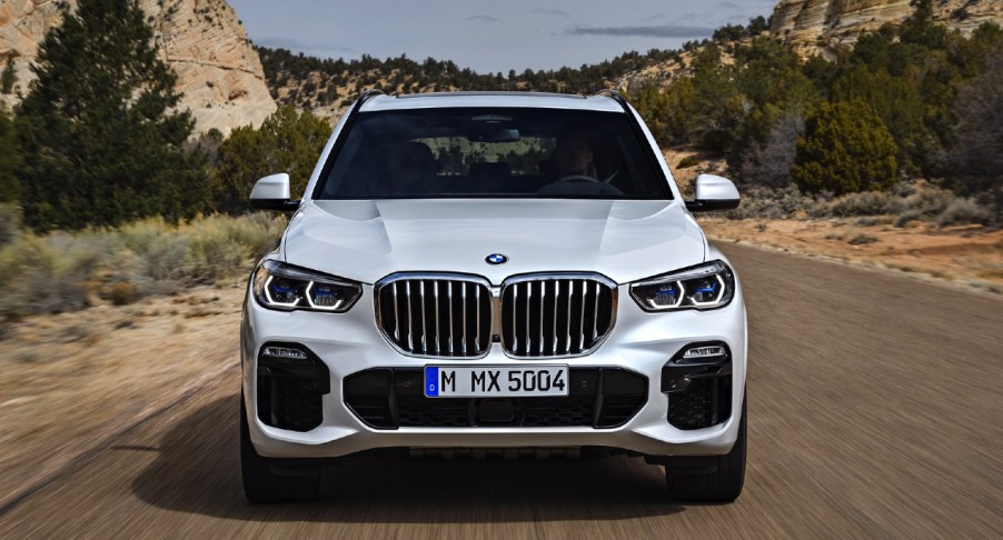 A white 2018 BMW X5 midsize luxury SUV is driving on the road.