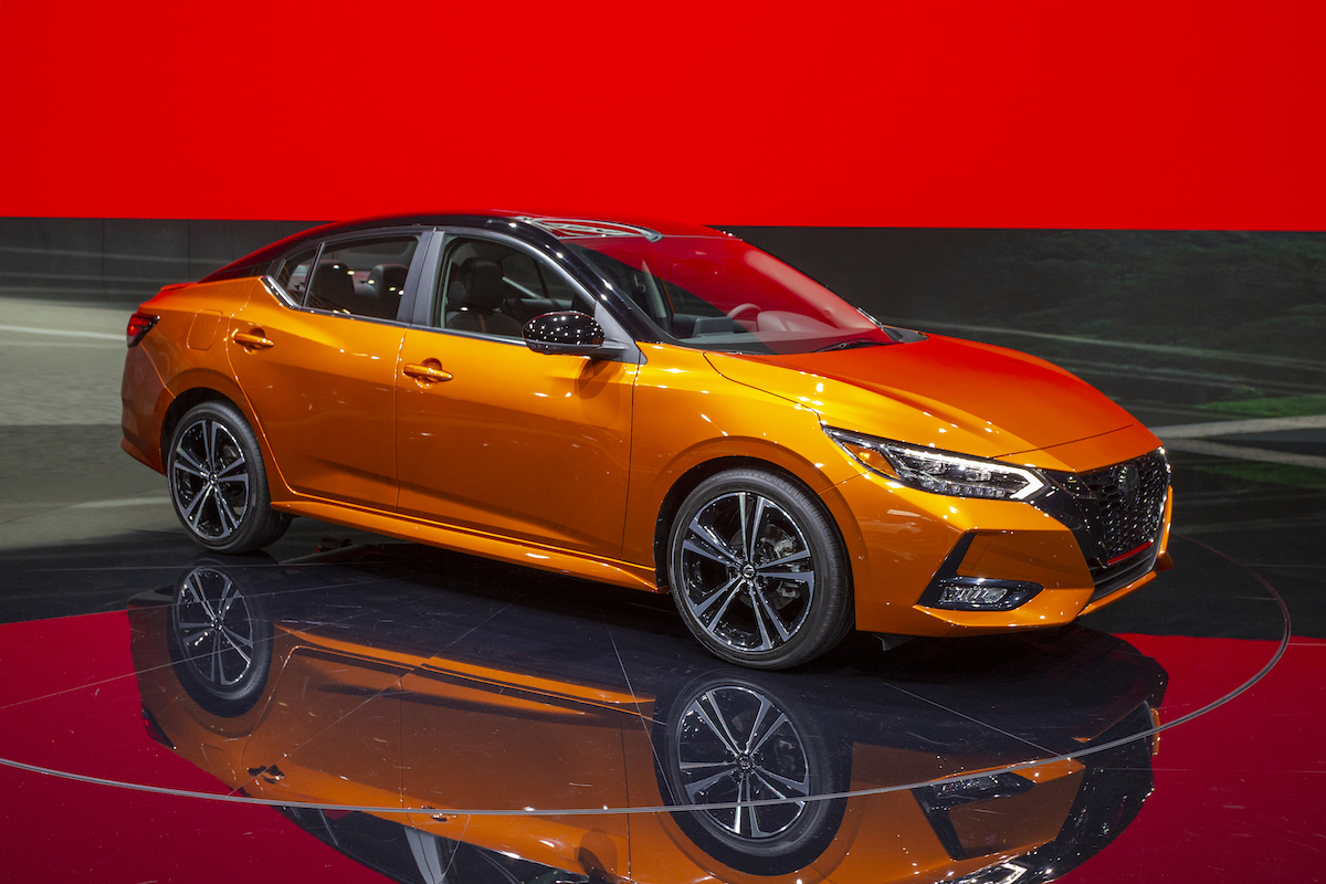 An orange 2019 Nissan Sentra in a showroom with black floors and red walls.