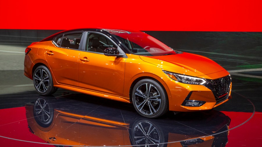 An orange 2019 Nissan Sentra in a showroom with black floors and red walls.