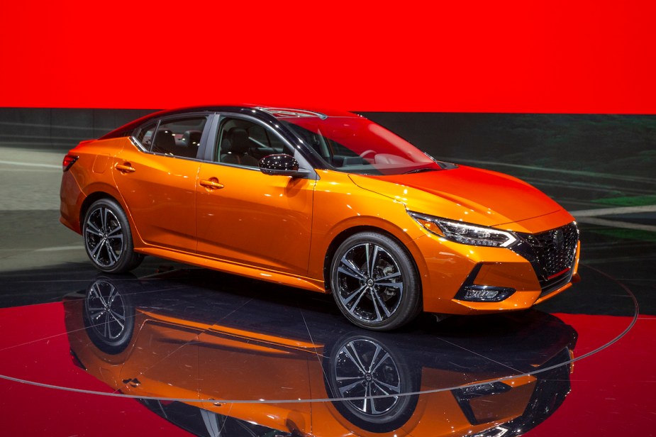 An orange 2019 Nissan Sentra in a showroom with black floors and red walls. 