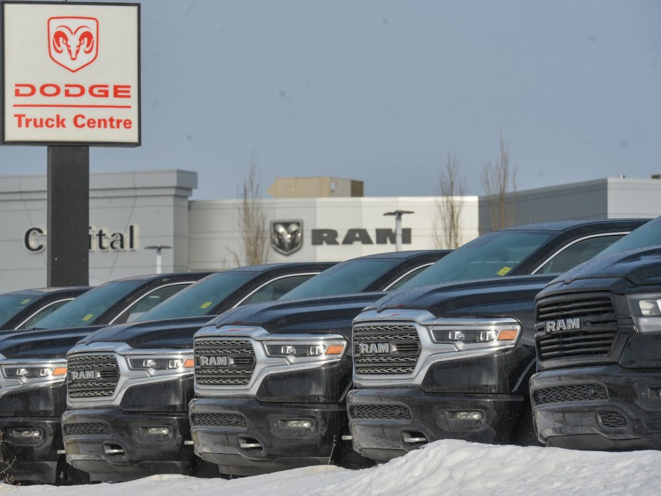 A row of new Ram pickup trucks parked in front of a Ram dealership, a snowbank visible in the foreground.