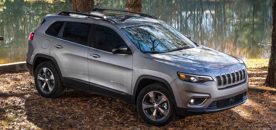 A silver 2022 Jeep Cherokee parked by a body of water in a forested area. 