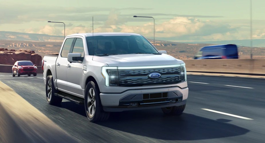A gray Ford F-150 Lightning electric pickup truck is driving on the road.