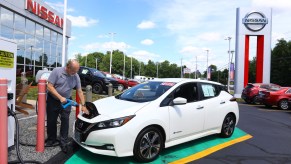 A dealer technician plugs a Leaf in to charge outside a Nissan dealership.