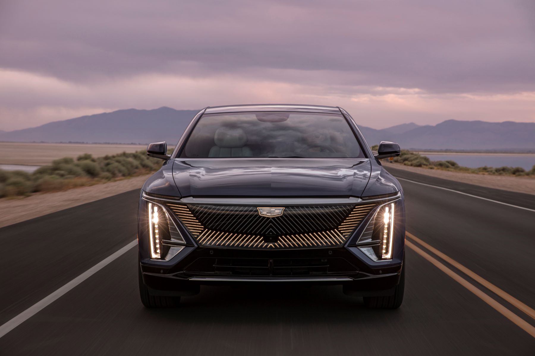 The grille and headlight configuration of a 2023 Cadillac Lyriq all-electric (EV) luxury SUV model on a highway