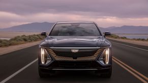 The grille and headlight configuration of a 2023 Cadillac Lyriq all-electric (EV) luxury SUV model on a highway