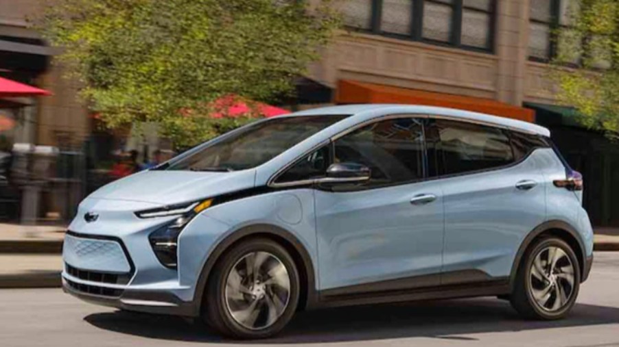 A blue 2023 Chevy Bolt EV electric hatchback is driving on the road.