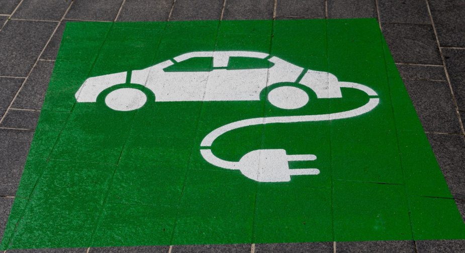 A green electric vehicle symbol painted on the pavement next to a rapid EV charger.