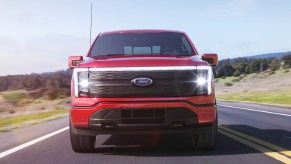 A red 2023 Ford F-150 Lightning electric pickup truck is driving on the road.