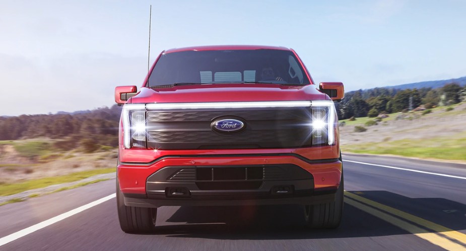 A red 2023 Ford F-150 Lightning full-size electric pickup truck sis driving on the road. 