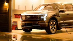 A gray 2023 Ford F-150 lightning electric pickup truck is charging in a garage.