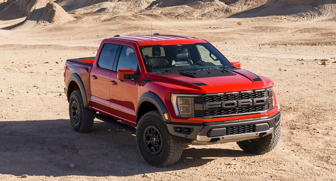 A red 2023 Ford F-150 Raptor full-size off-road pickup truck is driving off-road.