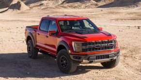 A red 2023 Ford F-150 Raptor full-size off-road pickup truck is driving off-road.