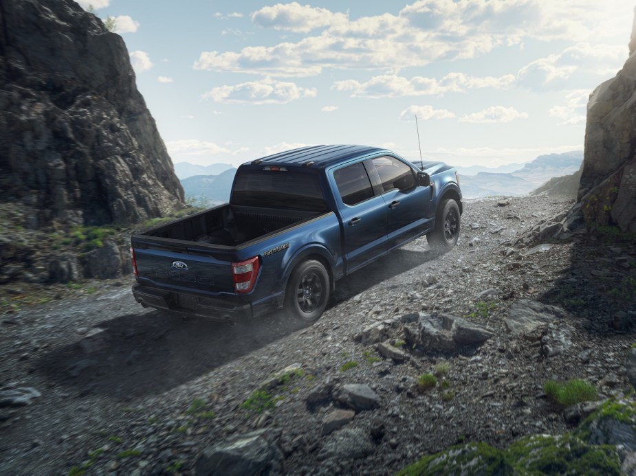 Blue Ford F-150 Fx4 Rattler parked in front of a mountain range, boulders visible in the background.
